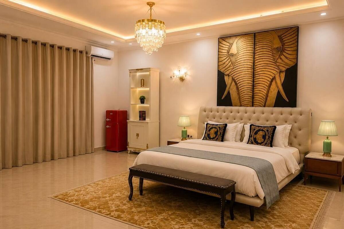 A bedroom with a large bed, a chandelier, a wall-mounted artwork, and a red cabinet.