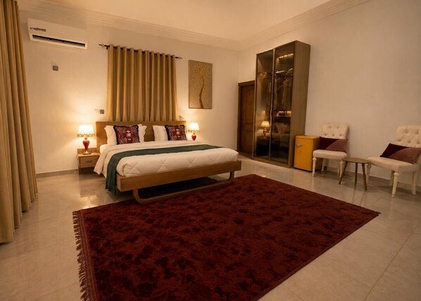 A bedroom with a bed, bedside lamps, a red rug, a wardrobe, and a chair.