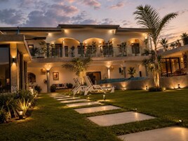 Un edificio de varios pisos con piscina, mobiliario exterior y un jardín bien iluminado.