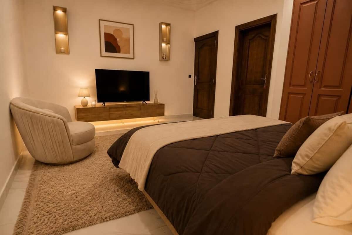 A bedroom with a bed, a chair, a TV, and a wardrobe.