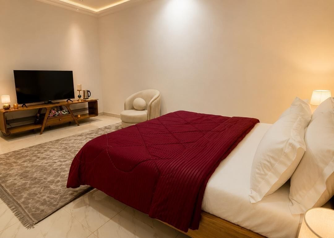 A bedroom with a bed, a TV, a chair, and a bedside table.