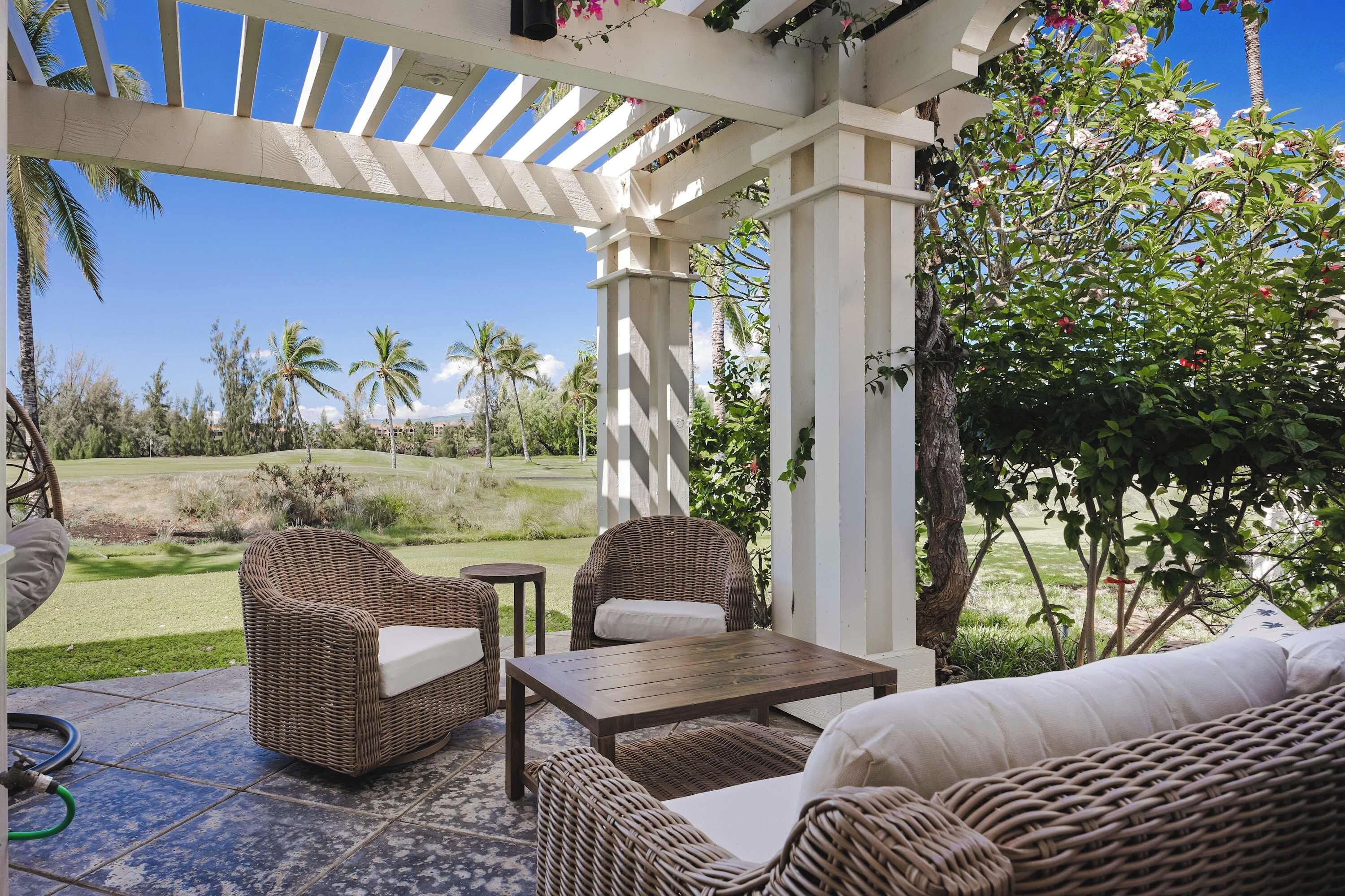 A covered outdoor seating area with wicker furniture and a view of a golf course.