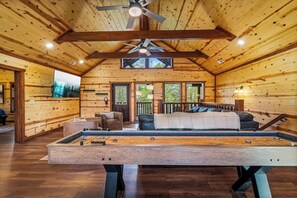 A spacious room with a pool table, wooden walls, and a ceiling fan.