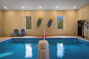 A swimming pool with two chairs and two surfboards on the wall. - 8BR Log Cabin | Indoor Pool + Outdoor Theater (Sevierville)