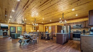 Un intérieur de chalet en bois spacieux, comprenant un coin repas, une cuisine et une cheminée.