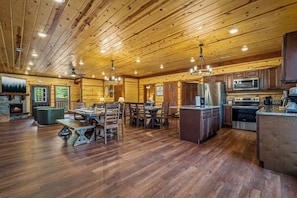 A spacious wooden cabin interior with a dining area, kitchen, and a fireplace. - 8BR Log Cabin | Indoor Pool + Outdoor Theater (Sevierville)
