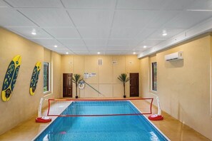 An indoor swimming pool with a net, surrounded by walls with doors and windows, and air conditioning units.