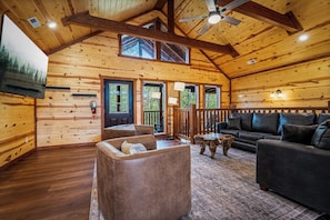 A log cabin interior with a wooden ceiling, a fireplace, a sofa, and a television.