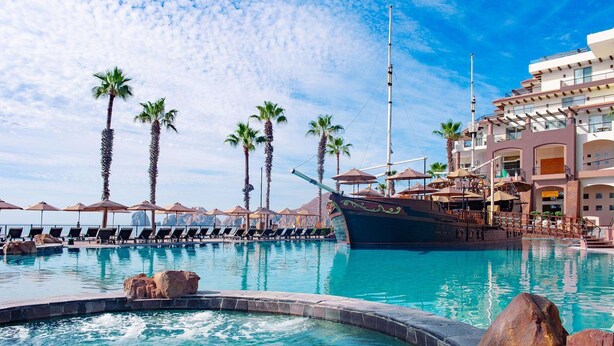 Ein Pool in einem Resort mit Liegestühlen, Palmen und einem Boot.