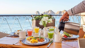 Ein Tisch mit Frühstücksangeboten, eine Karaffe zum Ausschenken und ein malerischer Blick auf Meer und Berge.