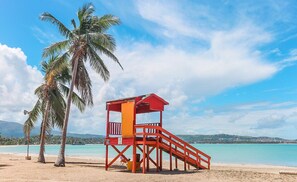 Ein Strand mit einem roten Rettungsturm, Palmen und klarem, blauem Wasser.
