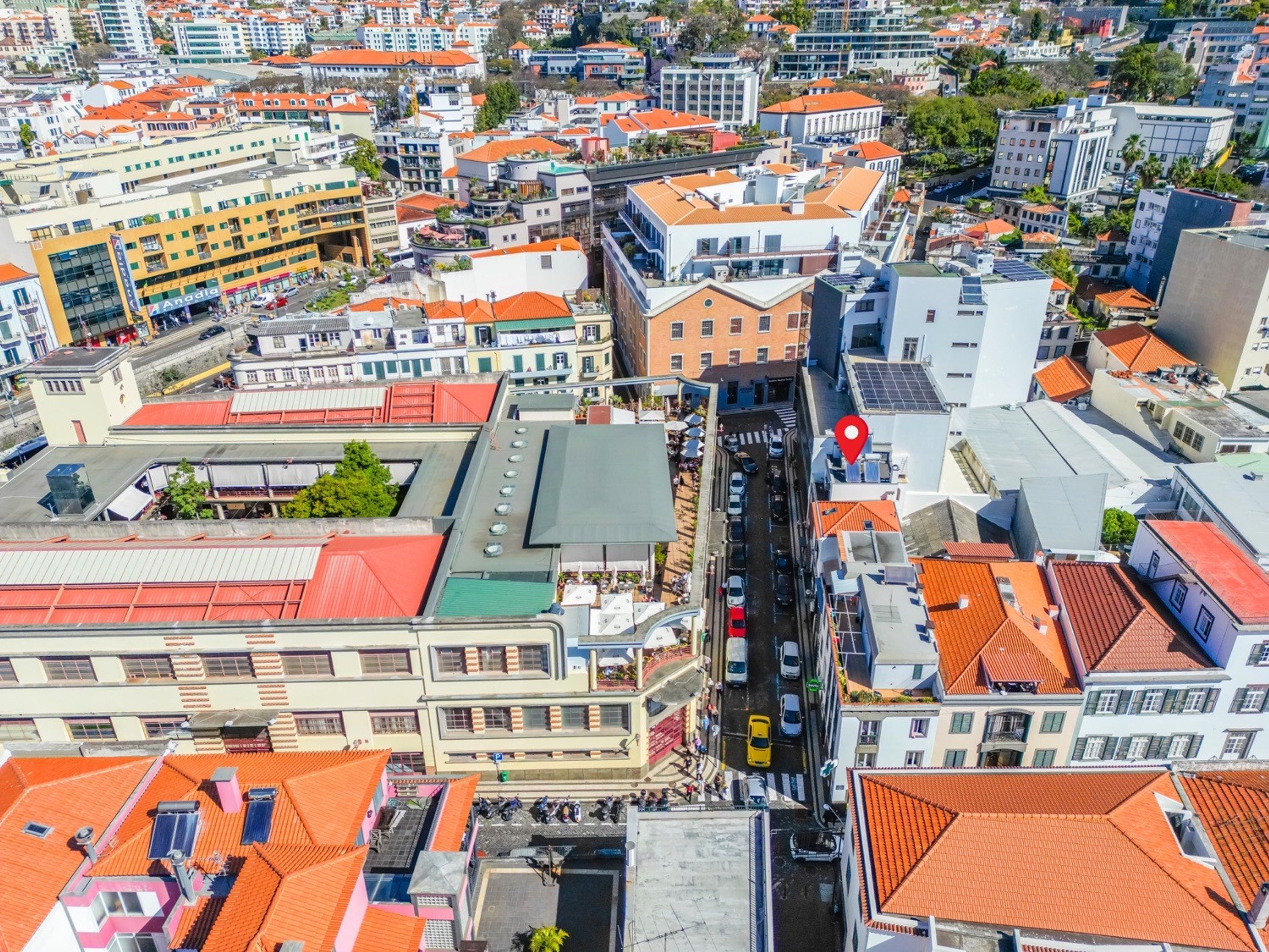 A high-rise building with a red roof, a central courtyard, and a street with cars.