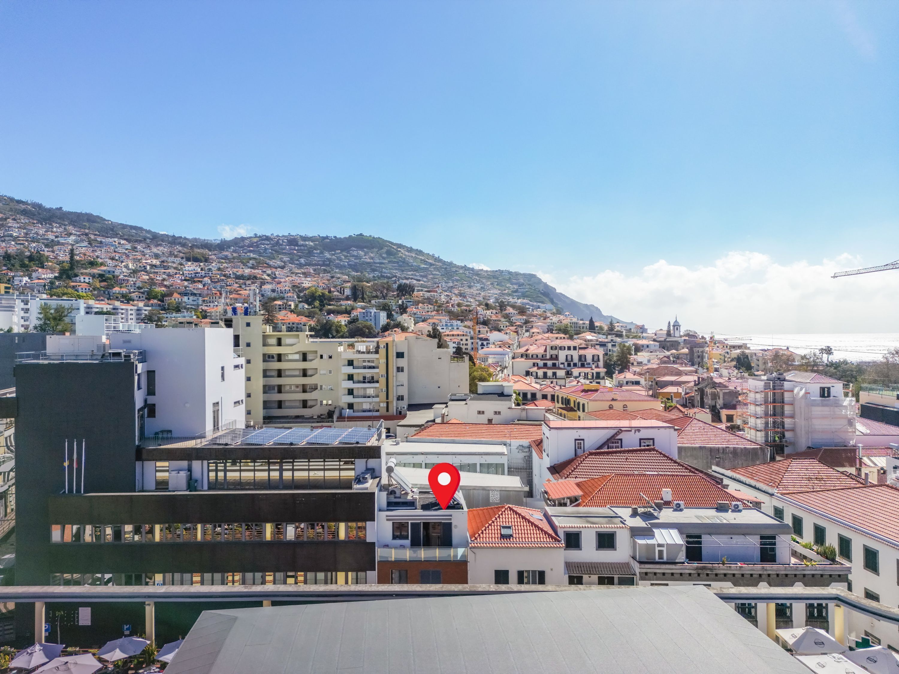 Une vue urbaine avec un repère rouge bien visible indiquant un lieu précis, des bâtiments modernes et un paysage vallonné en arrière-plan.