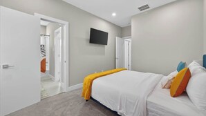 Ein Schlafzimmer mit einem Bett, einem an der Wand montierten Fernseher und einer Tür zu einem Badezimmer.