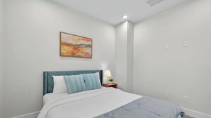Una camera da letto con un letto, un comodino, una lampada e un quadro appeso al muro.