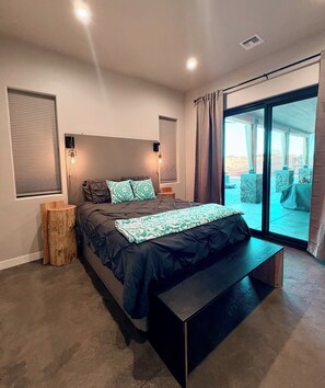 Ein modernes Schlafzimmer mit einem großen Bett, einer Bank, einem Nachttisch und Blick ins Freie.
