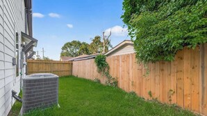 Ein Garten mit Holzzaun, Rasenfläche und Klimaanlage.