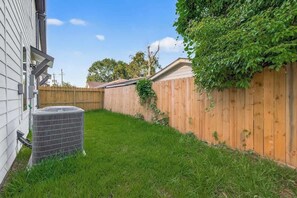 A backyard with a wooden fence, a grassy area, and an air conditioning unit. - Houston 3BR Home w/ Parking - Near Top Attractions (Houston)