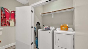 Un cuarto de lavandería con lavadora, secadora y un estante con productos de limpieza.