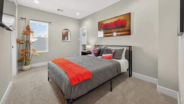 Un dormitorio con cama, mesita de noche, espejo, ventana con cortinas y un cuadro en la pared.