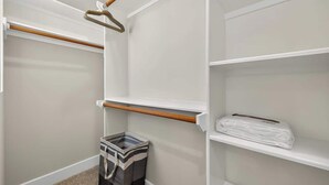 Un armario de vestidor con repisas abiertas, una barra para colgar ropa y un basurero.