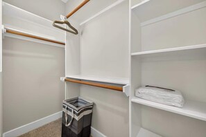Ein begehbarer Kleiderschrank mit offenen Regalen, einer Kleiderstange und einem Mülleimer.