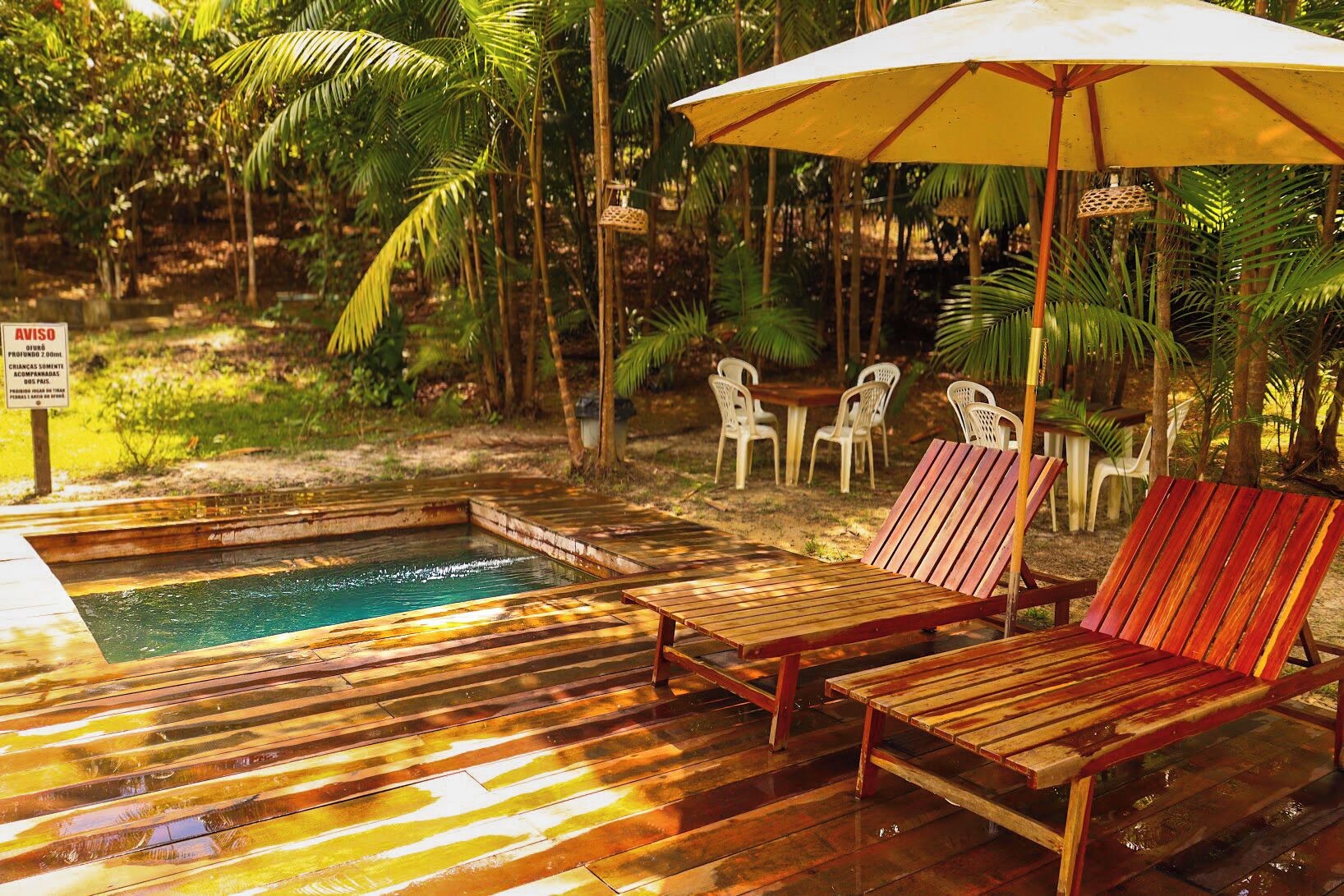 A wooden deck with a pool, lounge chairs, and an umbrella.