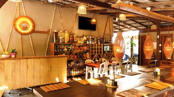 Zona de bar con muebles de madera, estantes con botellas y lámparas colgantes.