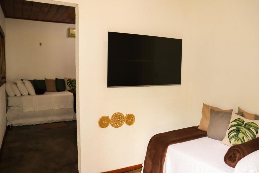 A room with a bed, a television mounted on the wall, and a sofa with cushions.