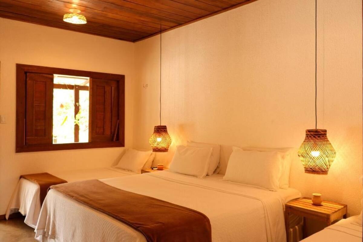 Un dormitorio con dos camas, cabecero de madera, una ventana con cortinas y dos lámparas de pared.