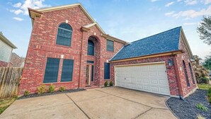 Une maison à deux étages en briques, avec un garage, une pelouse devant et un ciel dégagé.