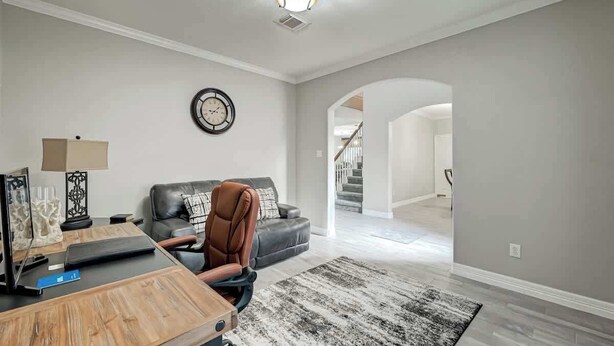 Un salon spacieux avec une table basse en bois, un canapé en cuir, une horloge noire au mur et un escalier menant à un autre niveau.