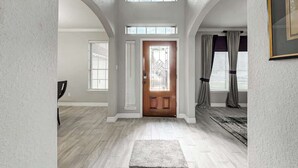 Un hall d’entrée spacieux, doté d’une porte en bois, d’un tapis et offrant une vue sur l’intérieur.