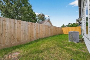 Ein Garten mit Holzzaun, Rasen und Klimaanlage.