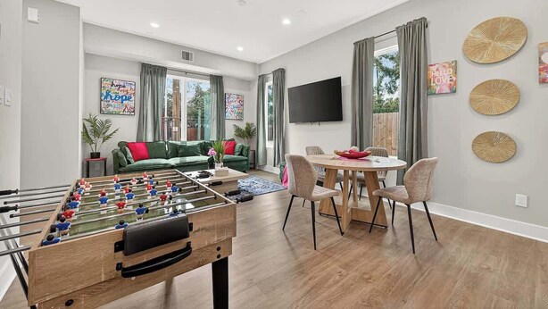 Een woonkamer met een tafelvoetbaltafel, een bank, een eettafel met stoelen en een aan de muur bevestigde televisie.