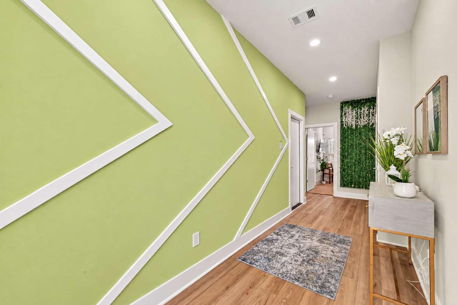 Un couloir aux murs verts, orné d’un tapis à motifs et doté d’un plancher en bois.