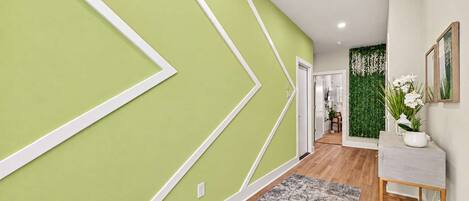 Un couloir aux murs verts, orné d’un tapis à motifs et doté d’un plancher en bois.