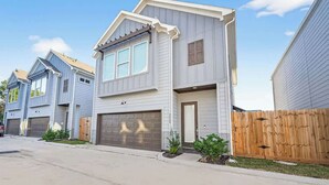 Een woonhuis met twee verdiepingen, een garage, een houten hek en een heldere lucht.