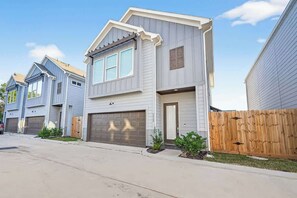 A two-story residential building with a garage, a wooden fence, and a clear sky.