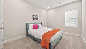 Een slaapkamer met een bed, een raam met zonwering, een aan de muur hangend schilderij en een vloerbedekking.