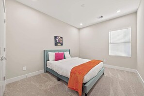 A bedroom with a bed, a window with blinds, a wall-mounted picture, and a carpeted floor.