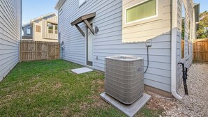 Een achtertuin met een huis, een houten schutting en een airconditioner.