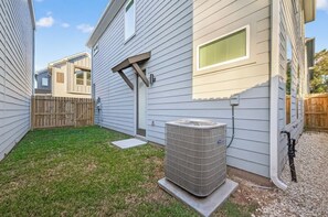 A residential backyard with a house, a wooden fence, and an air conditioning unit.