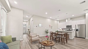 Een moderne keuken met witte kasten, roestvrijstalen apparatuur, en een eethoek met houten stoelen en een ronde tafel.