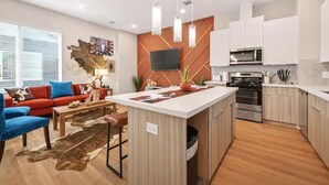 A modern kitchen with white cabinets, a central island, and a dining area with a red sofa and blue chairs. - Texas-Style 3BR Houston + Games (Houston)
