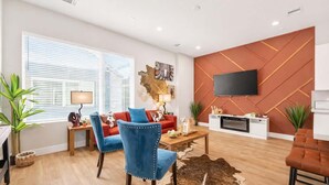 A modern living room with a sofa, chairs, a coffee table, a TV mounted on a wall, and a fireplace. - Texas-Style 3BR Houston + Games (Houston)