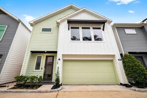 Ein zweistöckiges Haus mit Garage, Eingangstür und einer kleinen Veranda.