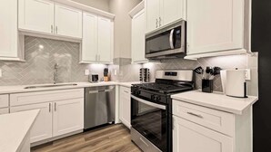 Une cuisine moderne avec des meubles blancs, des appareils en acier inoxydable et un dosseret de carrelage disposé en motif chevron.