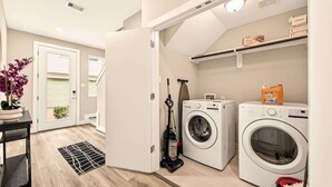 Une buanderie équipée de deux machines à laver, d’un aspirateur et d’une plante en pot.