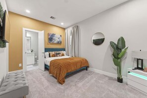 A bedroom with a bed, a bedside table, a mirror, a plant, and a wall-mounted artwork. - Tropical Jungle Home Escape & Retreat (Houston)